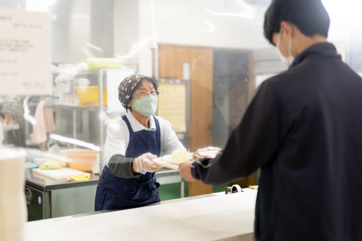 食堂スタッフが学生に食事を手渡す